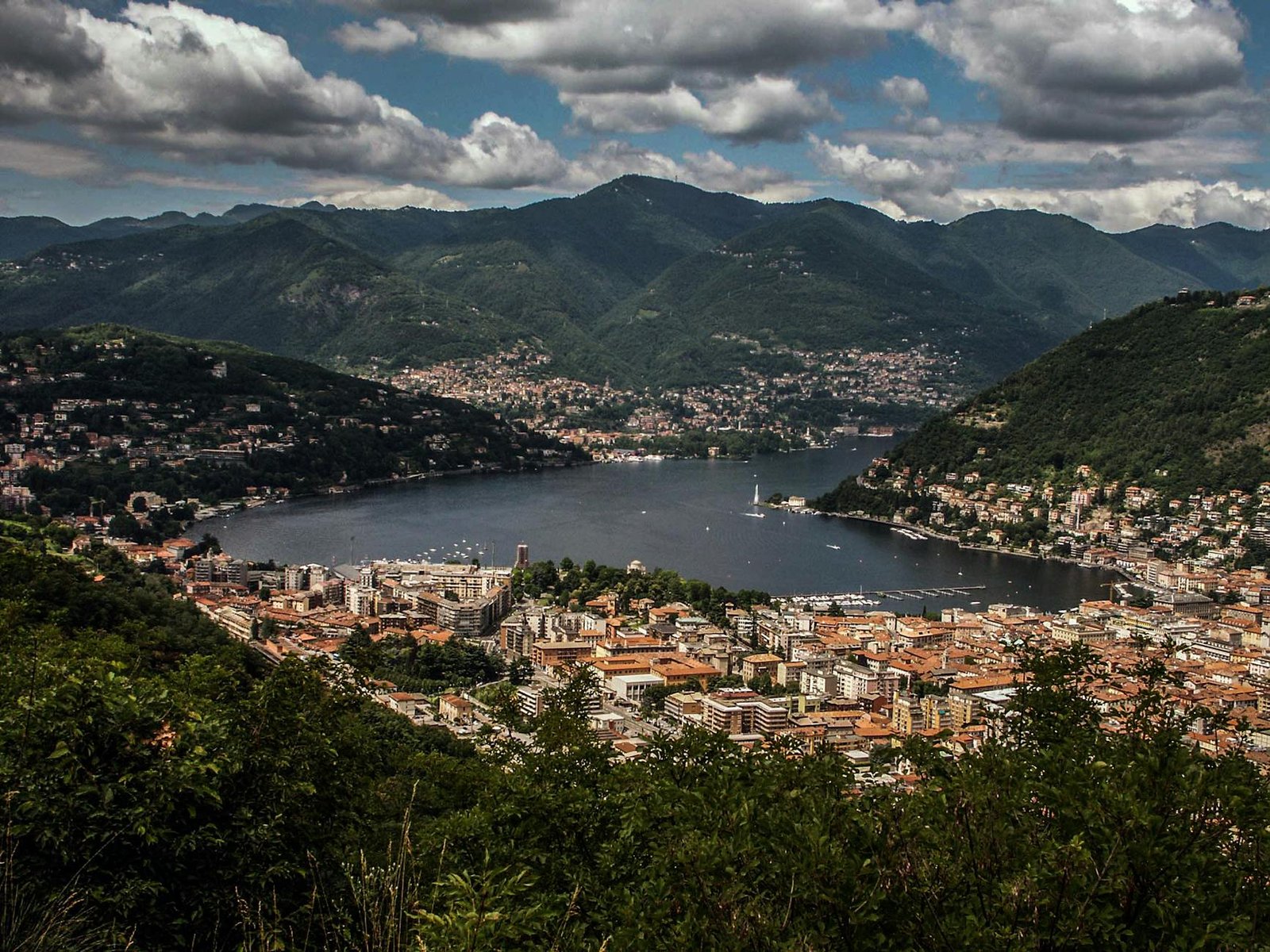 Aerial view of tranquil Lake Como surrounded by picturesque Lombardy mountains, showcasing nature's beauty.