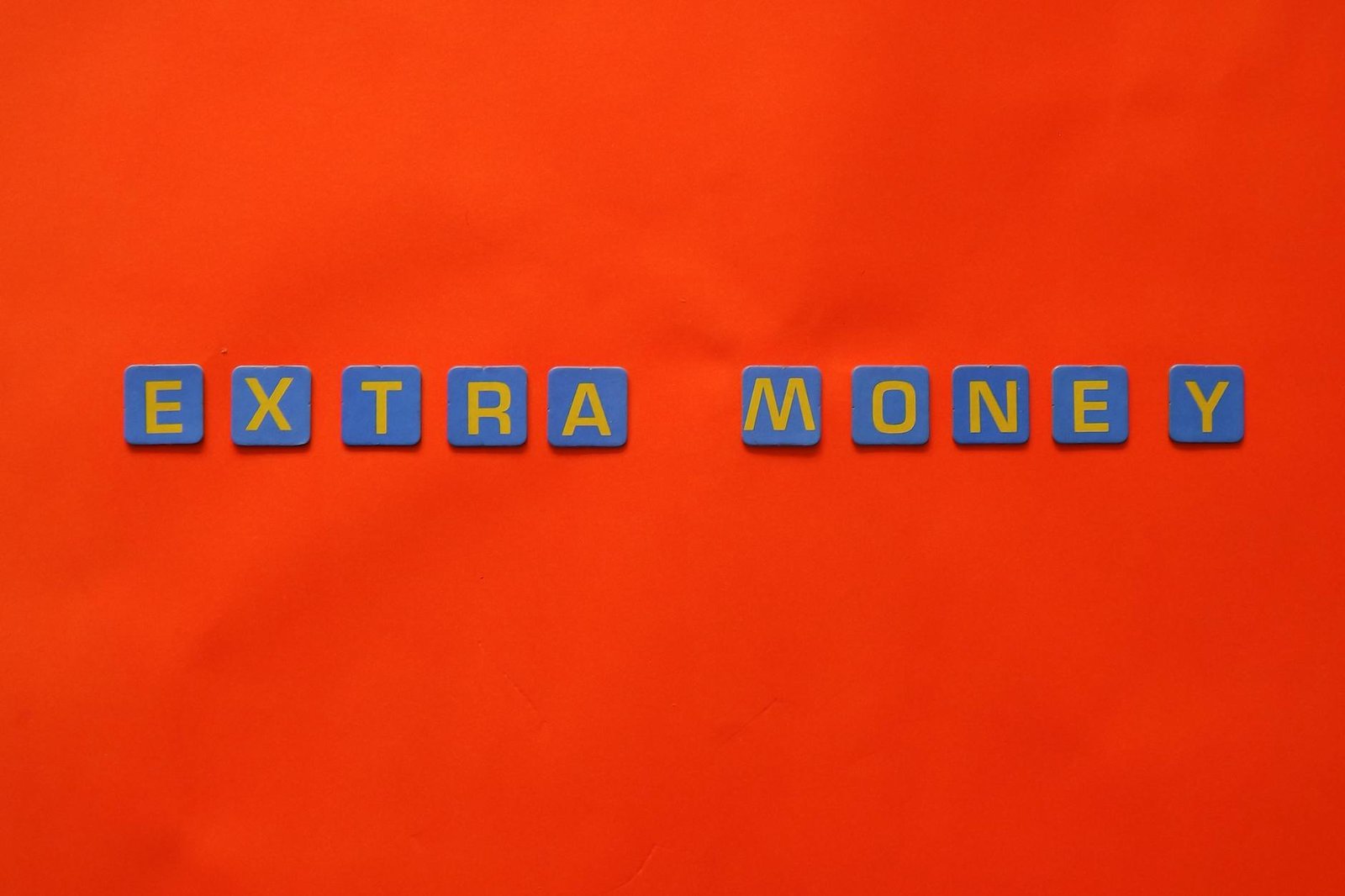 Bright orange background with 'EXTRA MONEY' in colorful tiles, symbolizing extra income ideas.