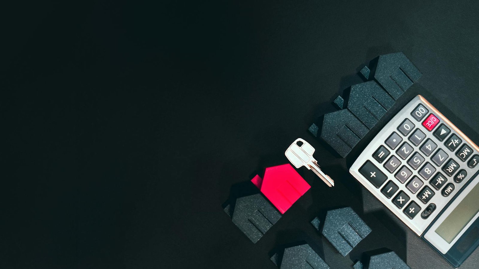 Calculator, houses, and a key symbolizing real estate investment concepts on a black background.