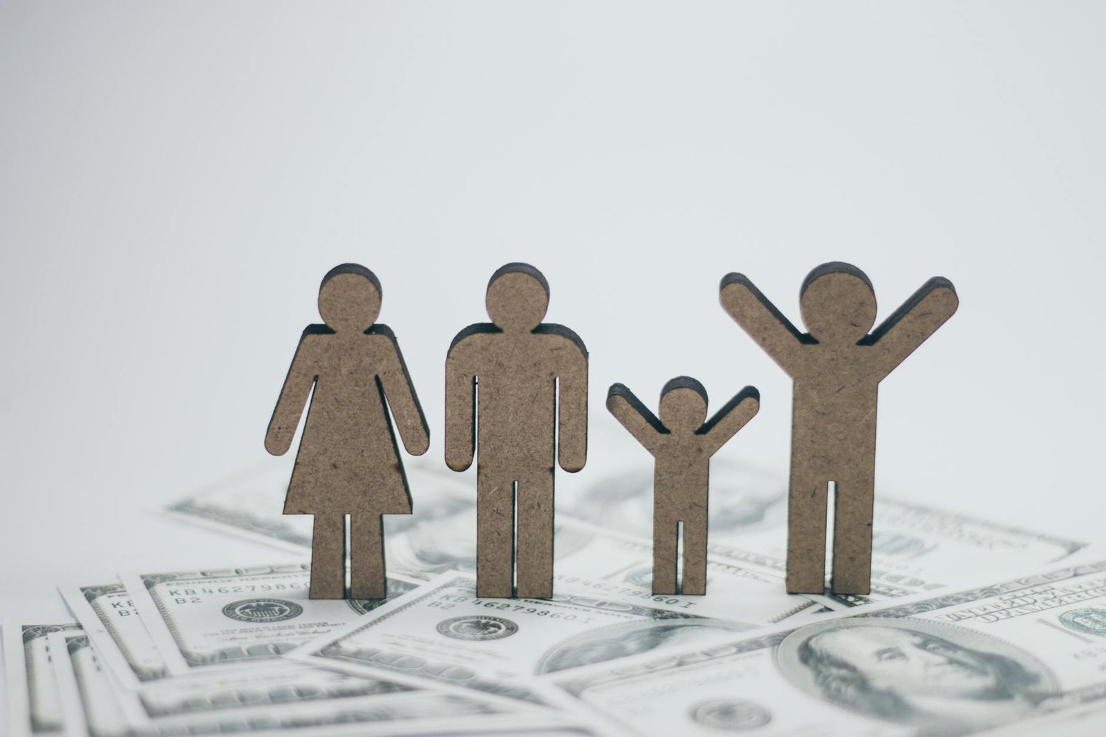 Wooden family figurines on dollar bills representing financial stability in family planning.